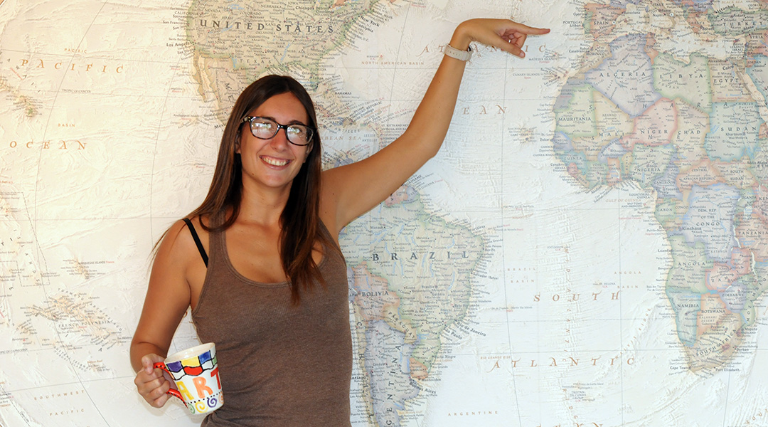 Larra Royo standing in front of a map of the world and pointing to Spain