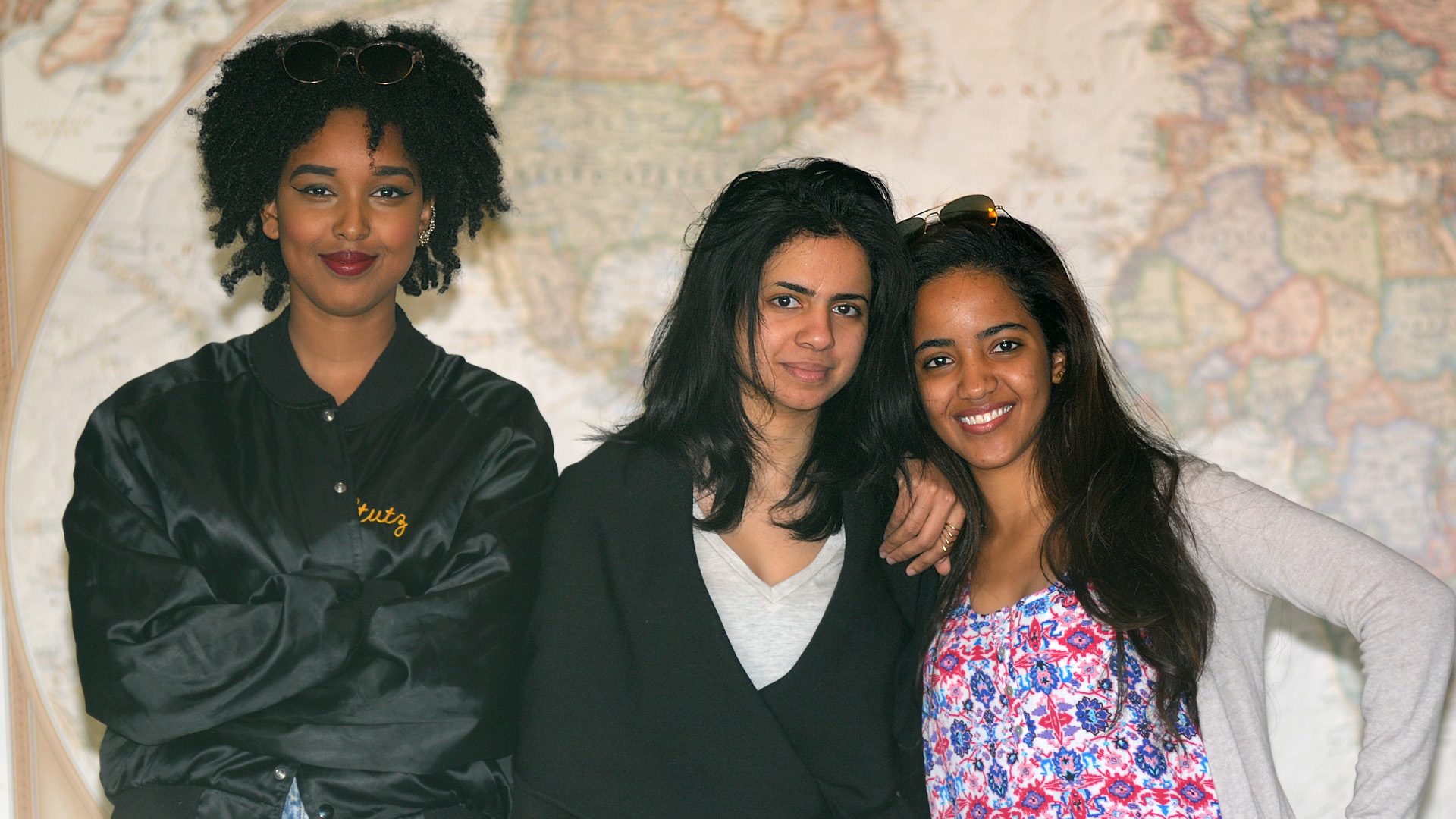 Hana, Shahad & Aisha stand in front of a large world map