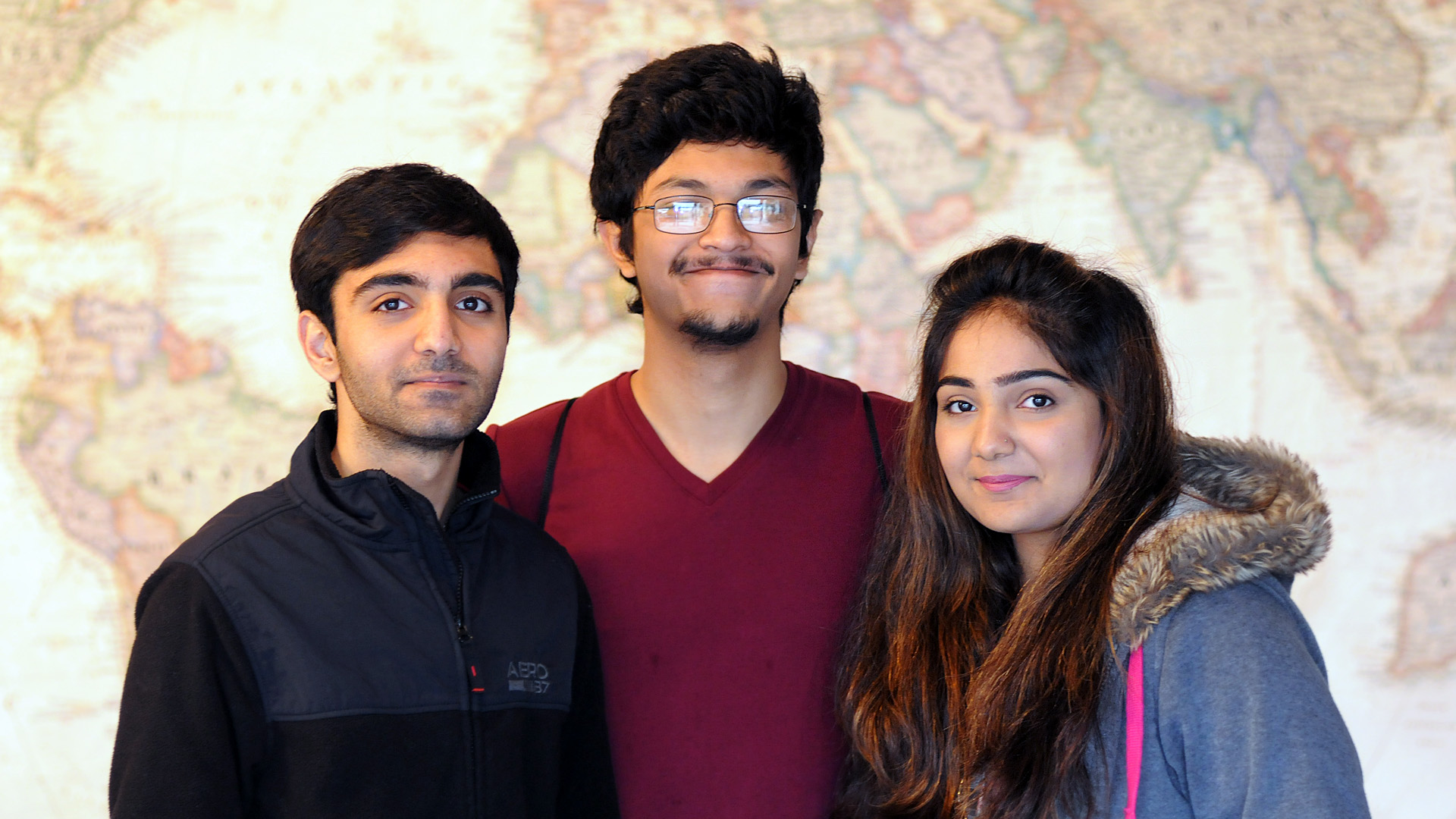 Waleed Ali, Saeef Alam & Sahar Ali standing in front of a large world map