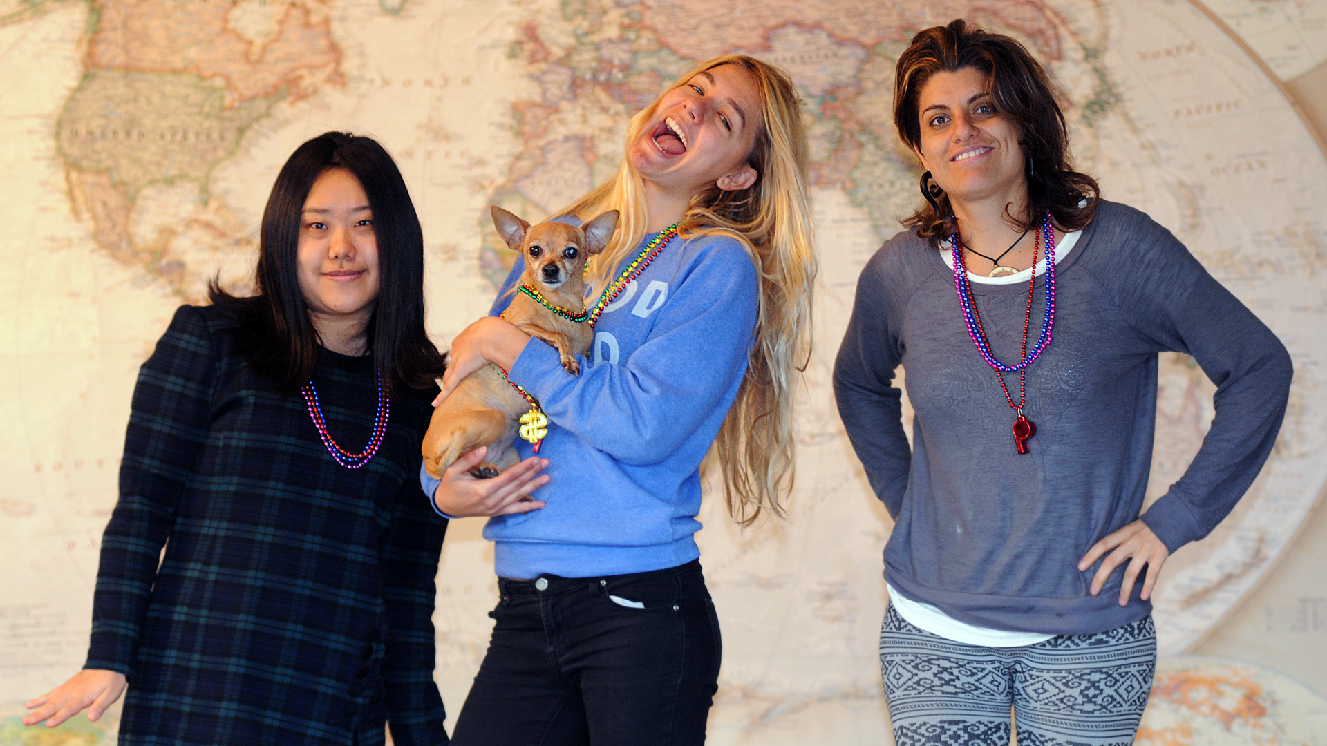 Blaire, Tiki, Dasha & Silvana in front of a large world map. They're all wearing "bling" like Mardi Gras beads