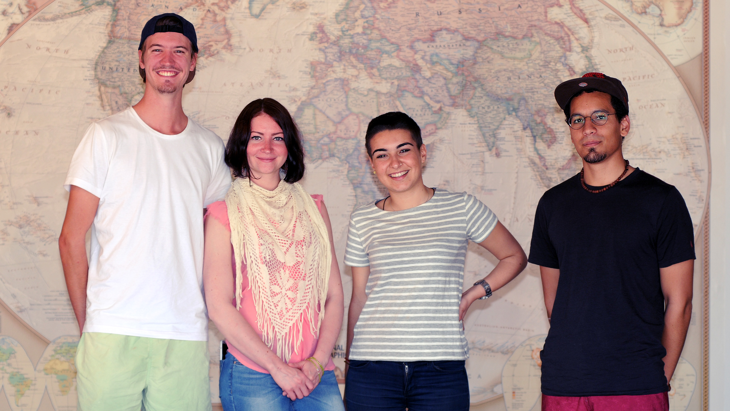 4 people standing in front of a large world map