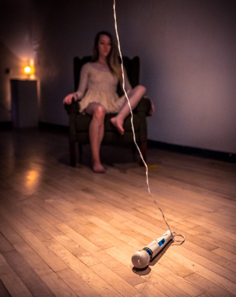 Photo of a vibrator on the gallery floor with a slightly out of focus Cortnee Brush in a chair in the background