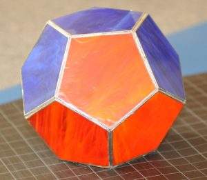 the Platonic Solid Dodecahedron made of blue and orange pentagons of stained glass