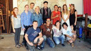 13 people posing for a group portrait in front of a large world map