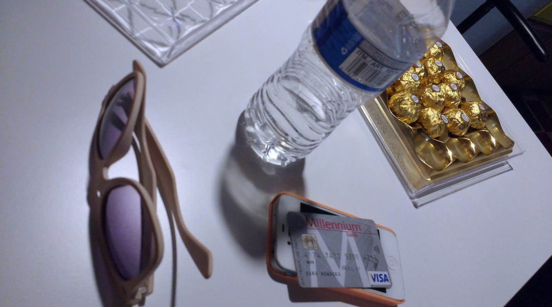 Sunglasses, iPhone, Credit Card, bottle of water, and box of chocolates on a table