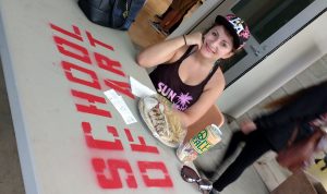 Elena sits at a "School of Art" table and eats lunch