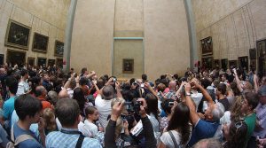 Photo from the back of the gallery at the Louvre in Paris showing hundreds of people trying to take cell phone pix of the Mona Lisa