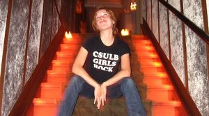 Christine M. Johnson sitting in a dark stairwell and wearing a t-shirt that reads "CSULB Girls Rock"