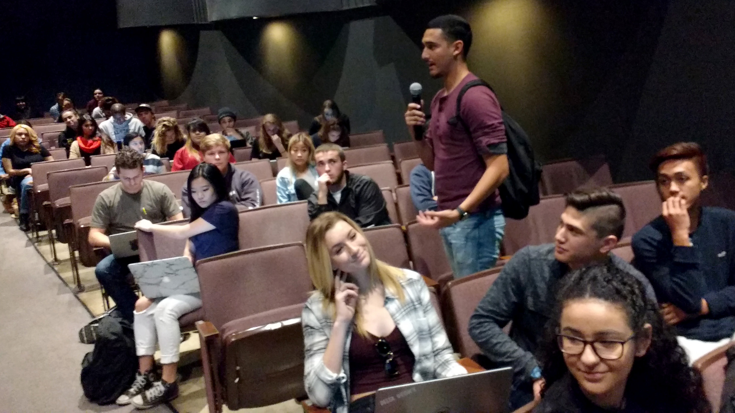 CSULB student holding a microphone and addressing the class in the University Theater