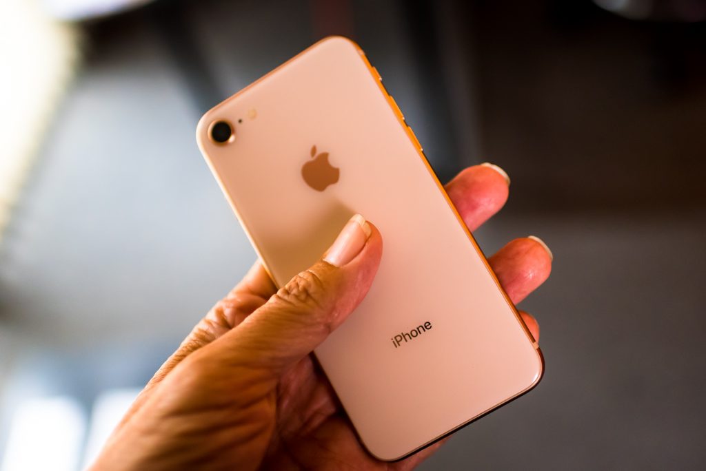 photo of a hand holding a gold iPhone 8 and showing the glass back of the handset