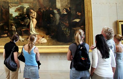 group of contemporary students, wearing denim, tank tops, back packs, looking at Courbet's 1855 painting Studio of a Painter