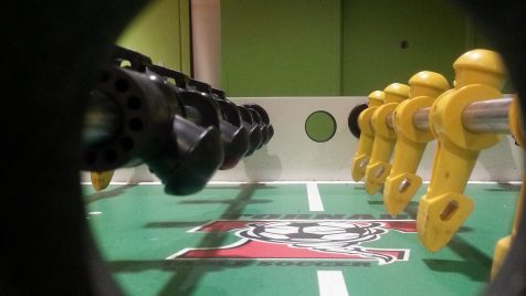 Photo of a Foosball table with the camera lens in the midfield hole for dropping the ball, so the feeling is of a "player level view" of the field