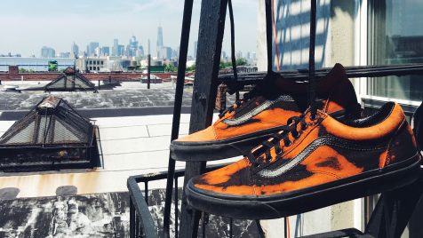 A pair of black and orange tennis shoes hanging from the fire escape outside an apartment building in New York City with towers and other buildings in the distance