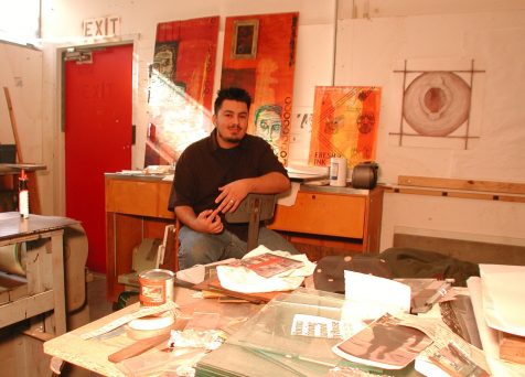 Matthew Rodela sitting in a printmaking space and surrounded by fine art prints on paper