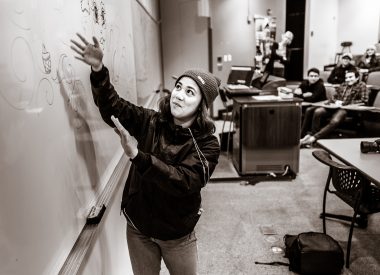 Filmmaker Audrey Resella gesturing to a whiteboard drawing as she tells the story of a mural