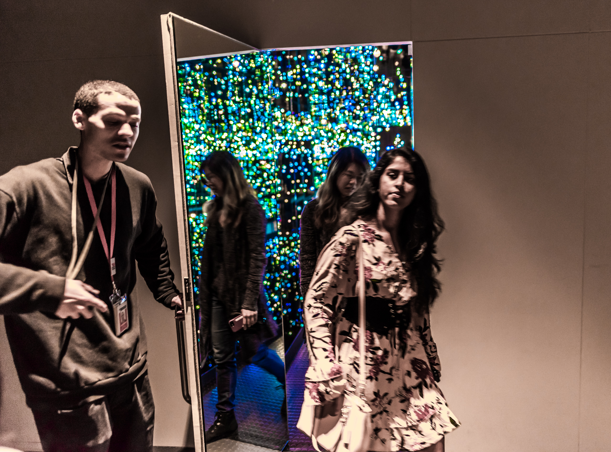 A visitor services associate holds a door open for people leaving one of Yayoi Kusama's infinity rooms