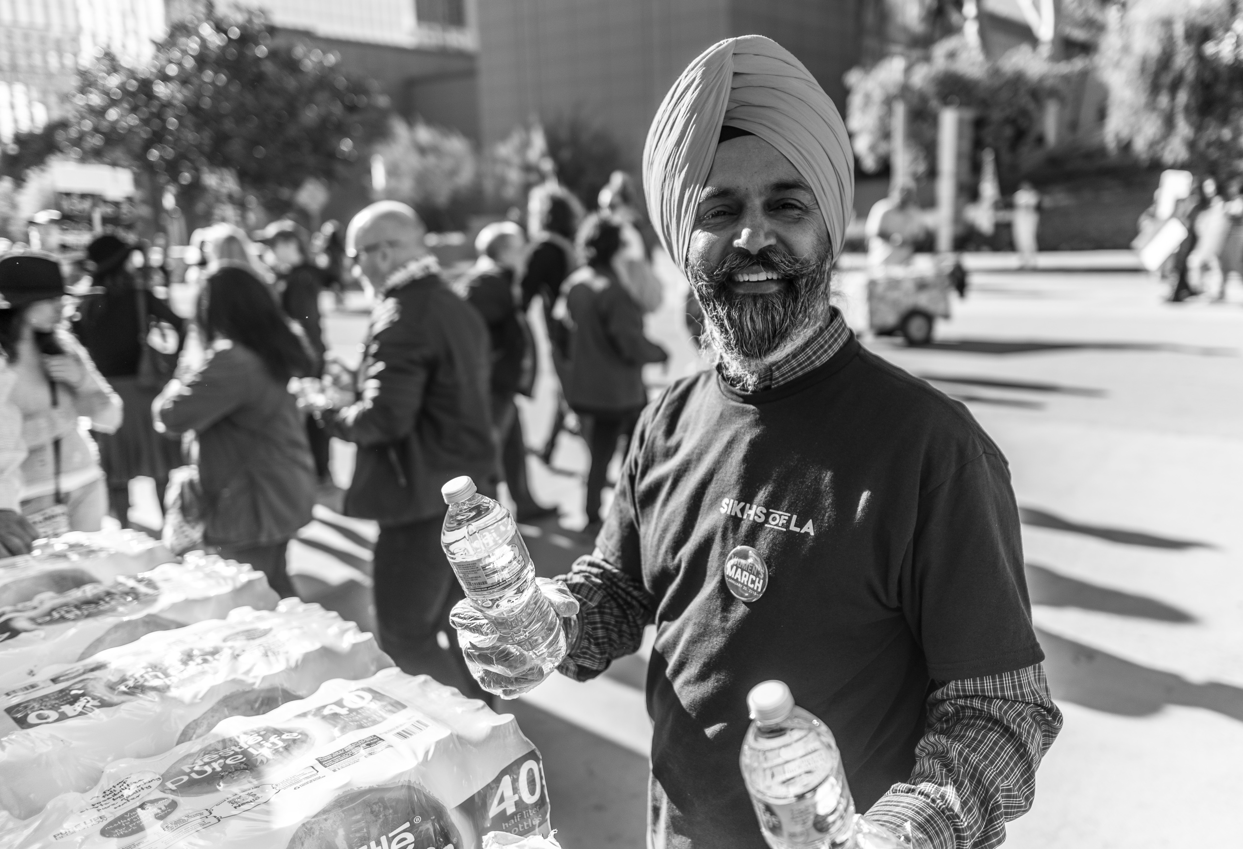 a man in a Sikhs of LA t-shirt and wearing a Women's March button hands out bottles of water to participants in the Women's March Los Angeles 2018