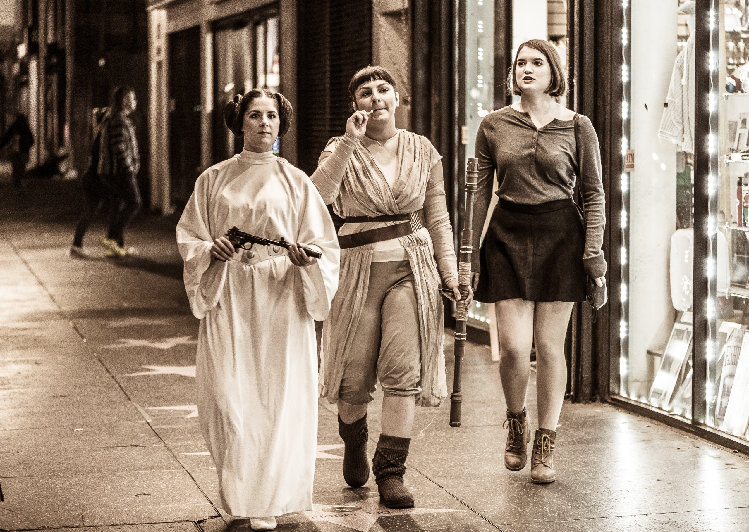 a woman cosplaying as Princess Leia, a woman dressed as Rey, and a third woman, not in costume, stroll down Hollywood Blvd.