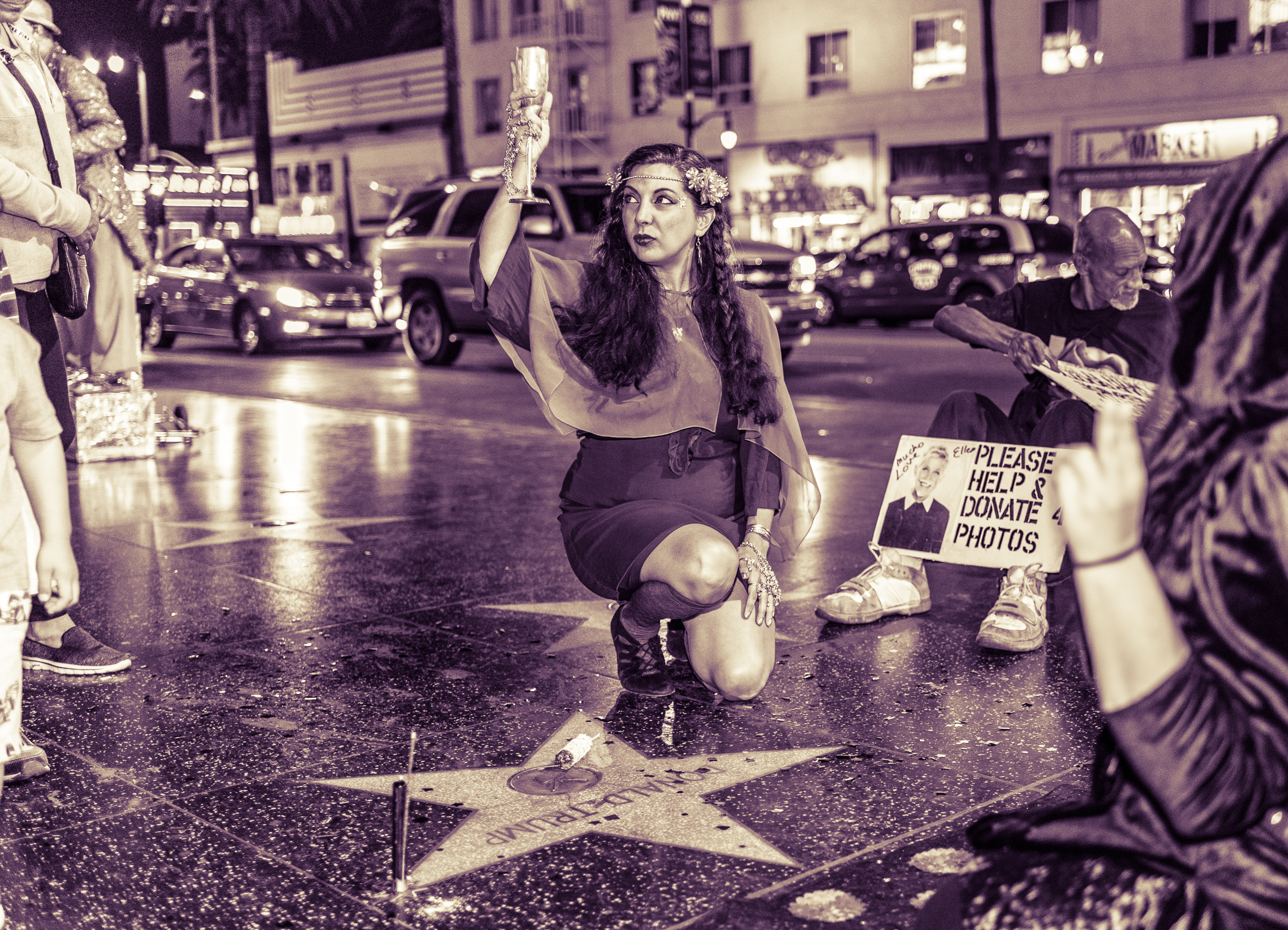 sepia-toned photograph of Darcey Leonard kneeling at Donald Trump's star on Hollywood and raising a goblet in the air above the star