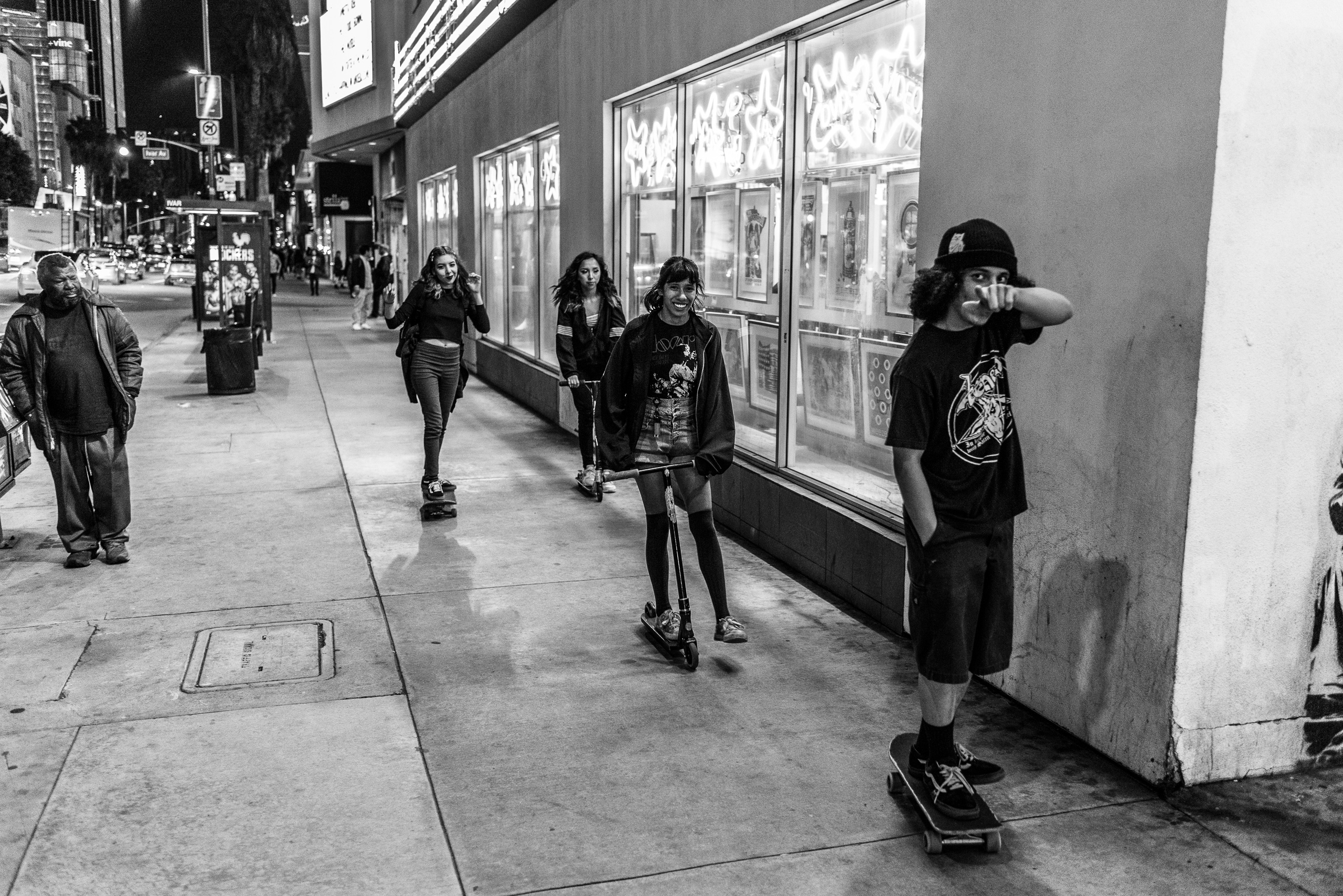 a guy and three girls skate down Sunset Blvd in Hollywood in front of Amoeba Music