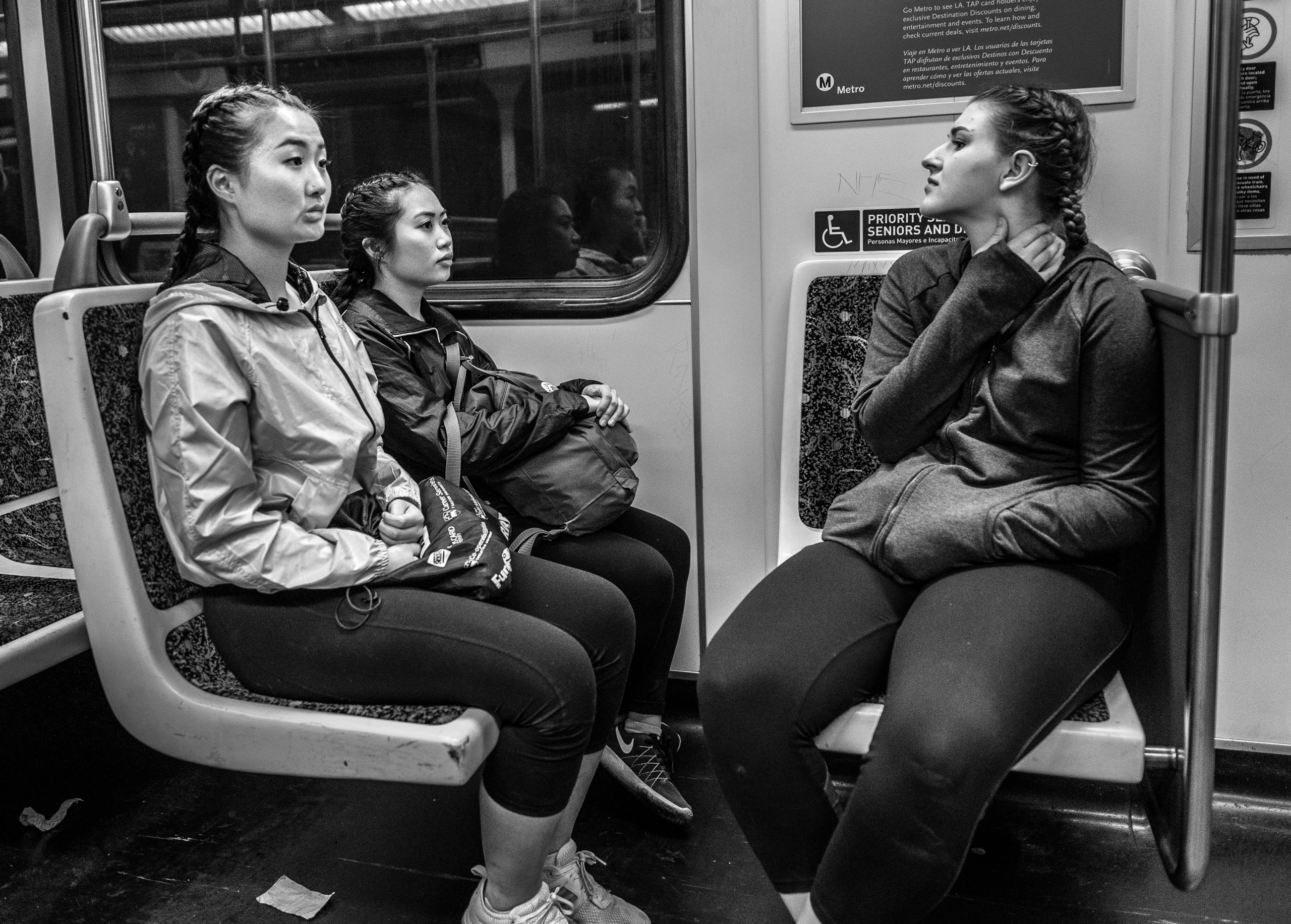Three women sit in a Los Angeles Metro Red Line train car and avoid making eye contact with the center aisle of the train