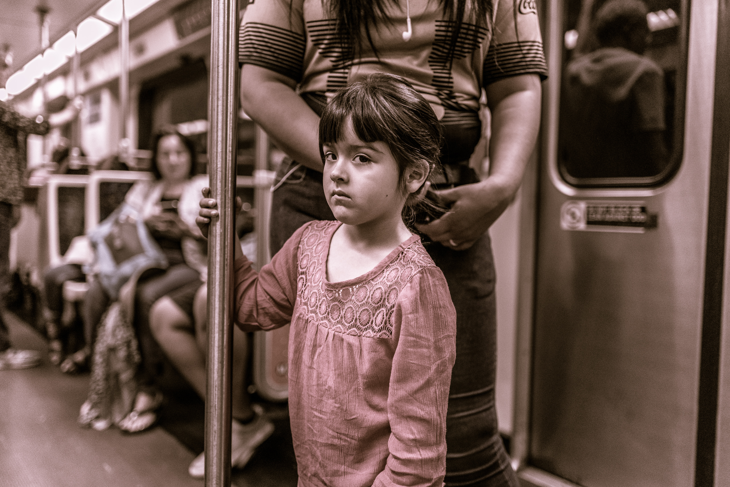 a young girl stands in the middle of a Metro train car as her mom pulls her hair back to put it in a ponytail