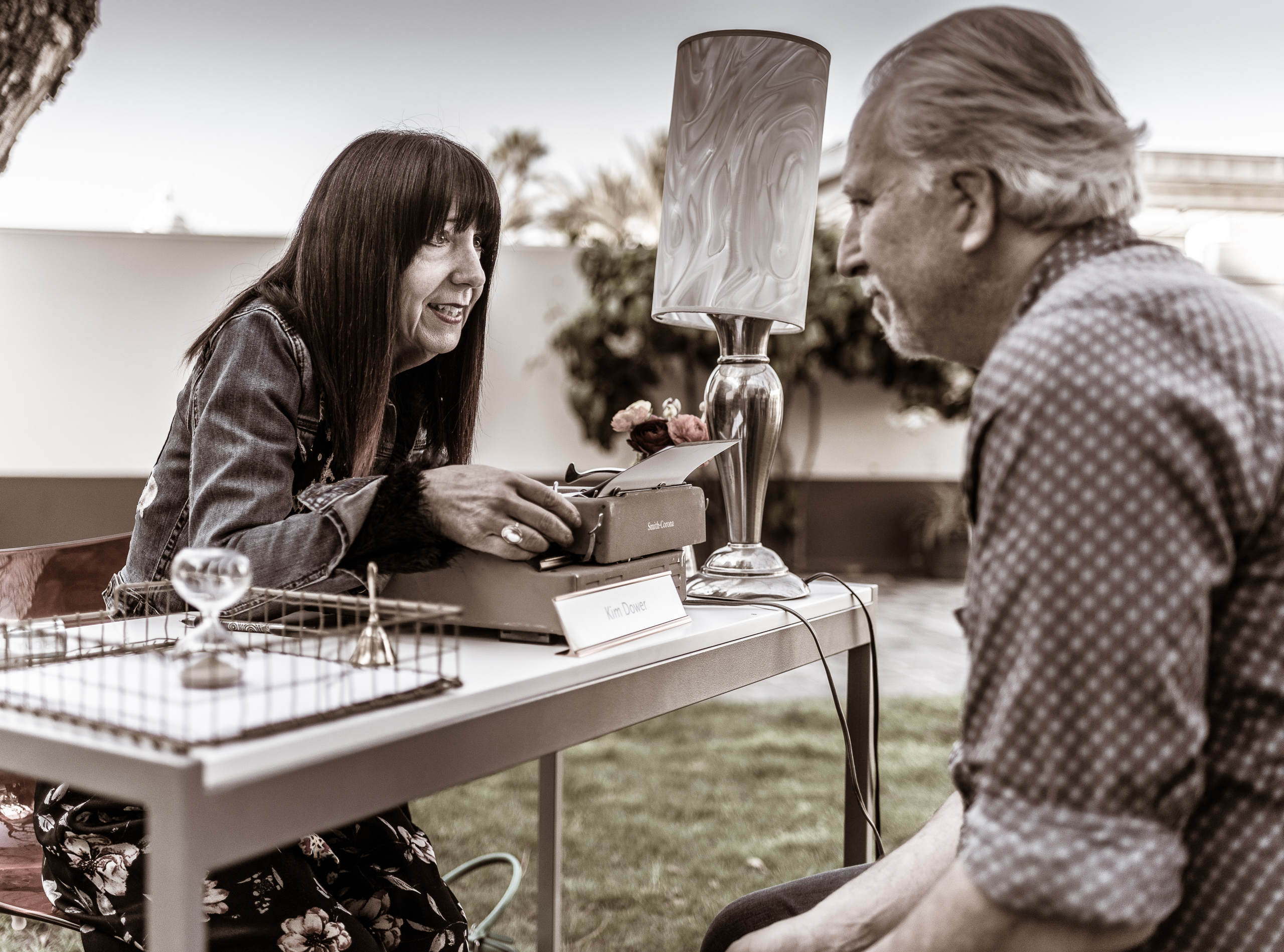 a poet and a guest sit across a table on the North Patio at Union Station in Los Angeles. As part of "The Poet is in" for National Poetry Month, poets have a conversation with a guest and then write a poem for them.