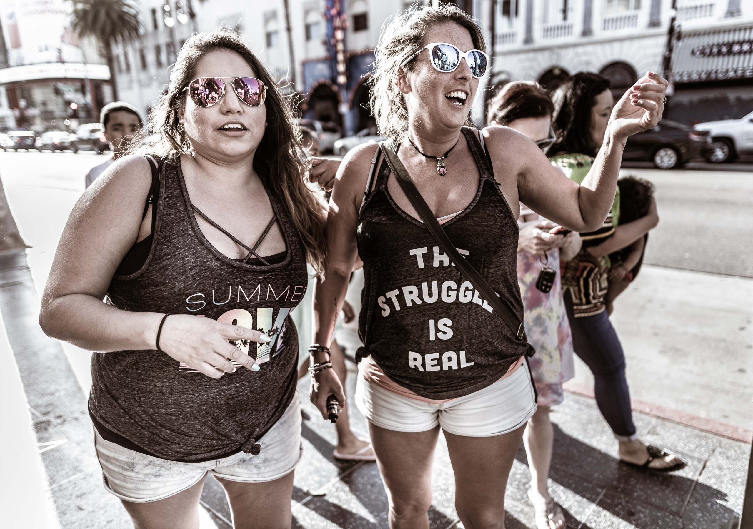 two women on Hollywood Blvd. The  first wearing a tank top that reads "Summer Love" and the second wearing a tank top that reads "the struggle is real"