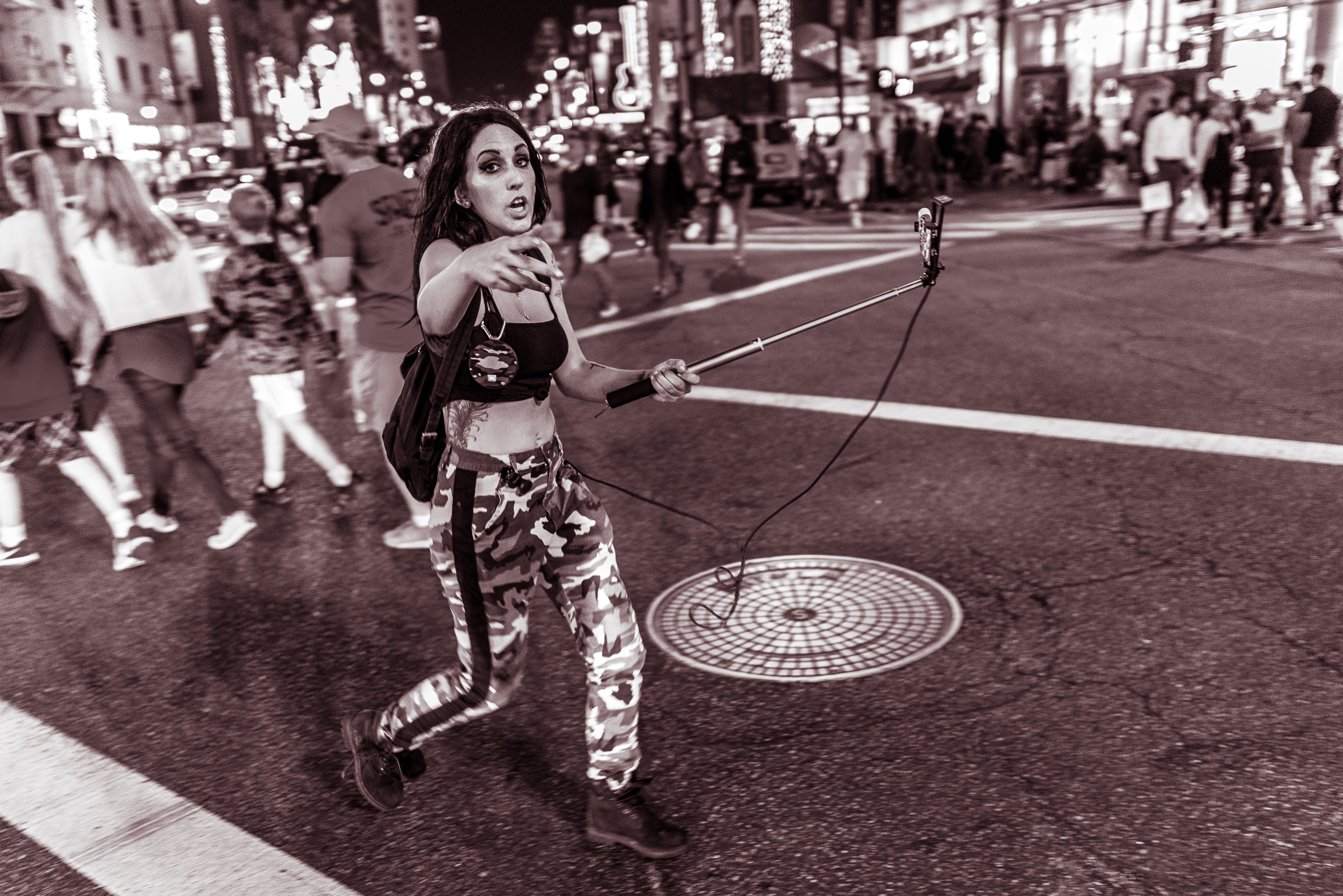 a woman crossing the 4-way intersection at Hollywood & Highland and talking into a cell phone on the end of a selfie-stick