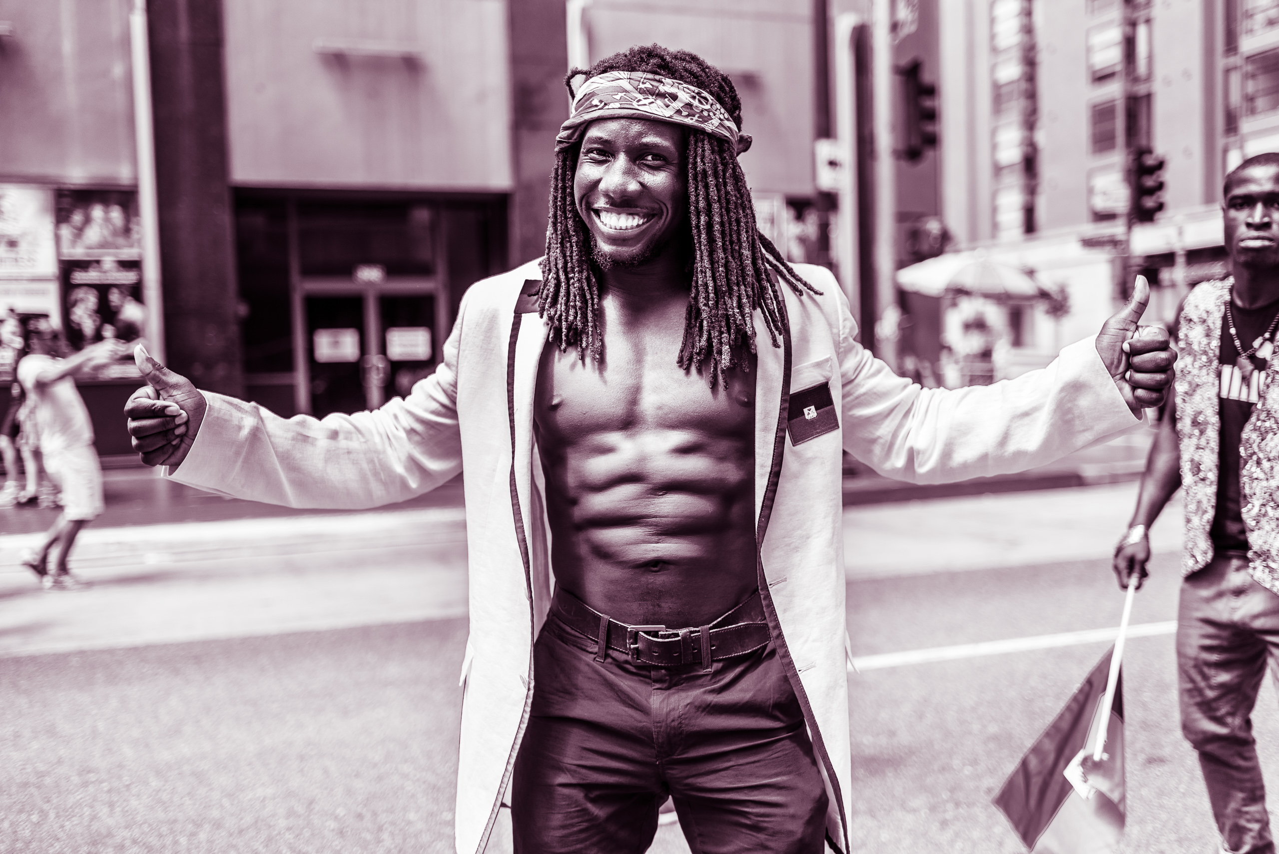 a guy in a white, linen Haiti jacket, pants, no shirt, and amazing abs holds his arms outstretched with two big thumbs up signs and a huge smile