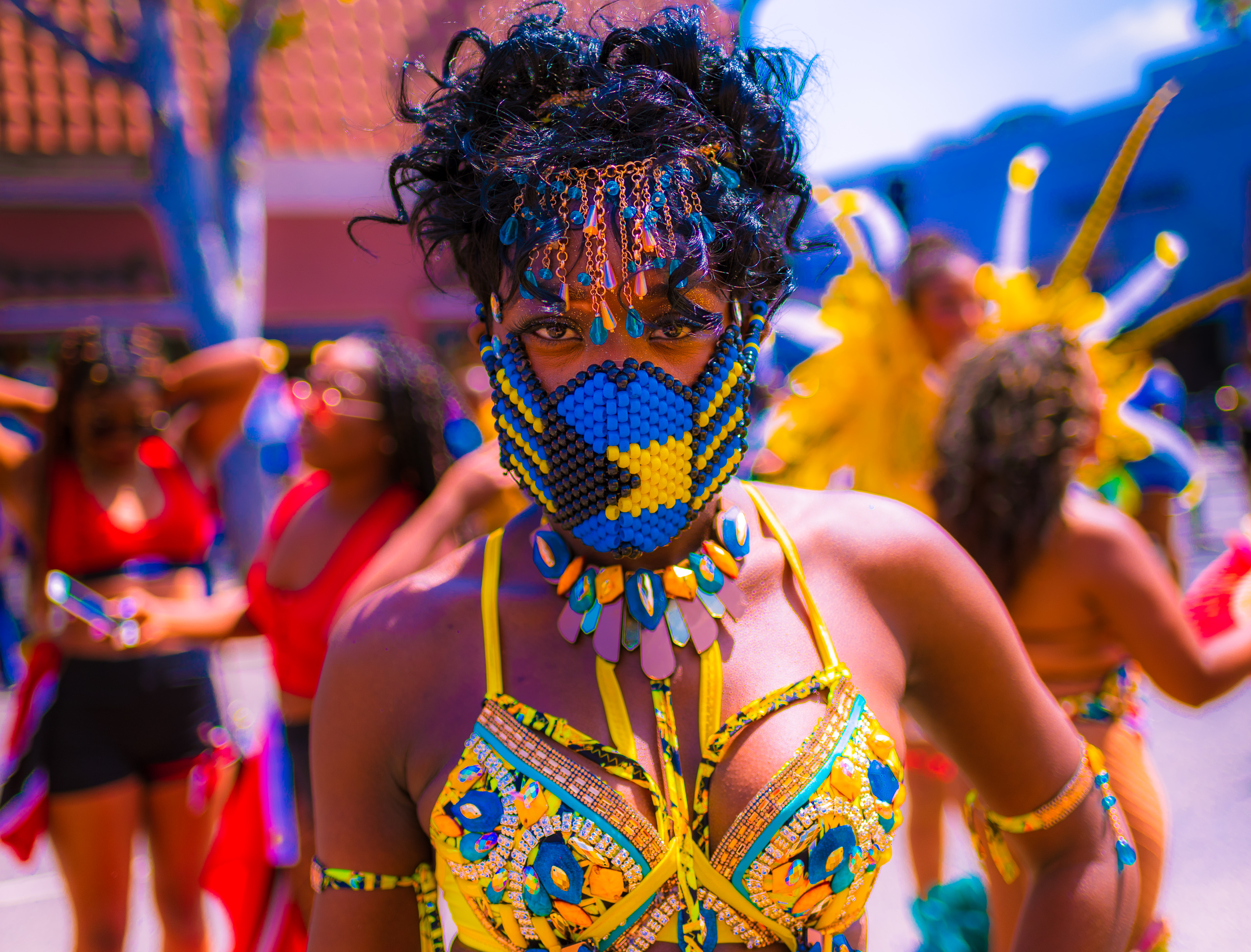a sun-drenched dancer in a vibrant costume and a Bahamas-flag mask