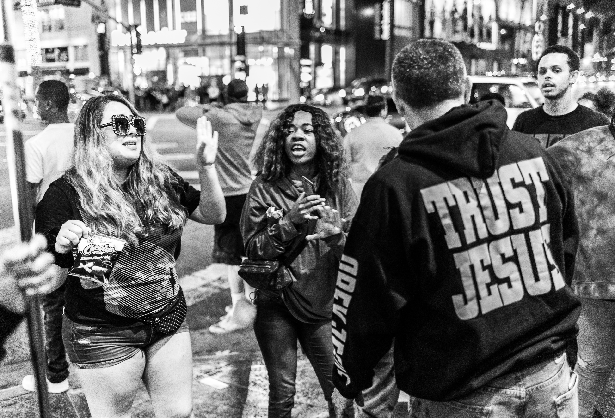 a woman with rhinestone sunglasses has a shouting match with a preacher in a "trust Jesus" hoodie