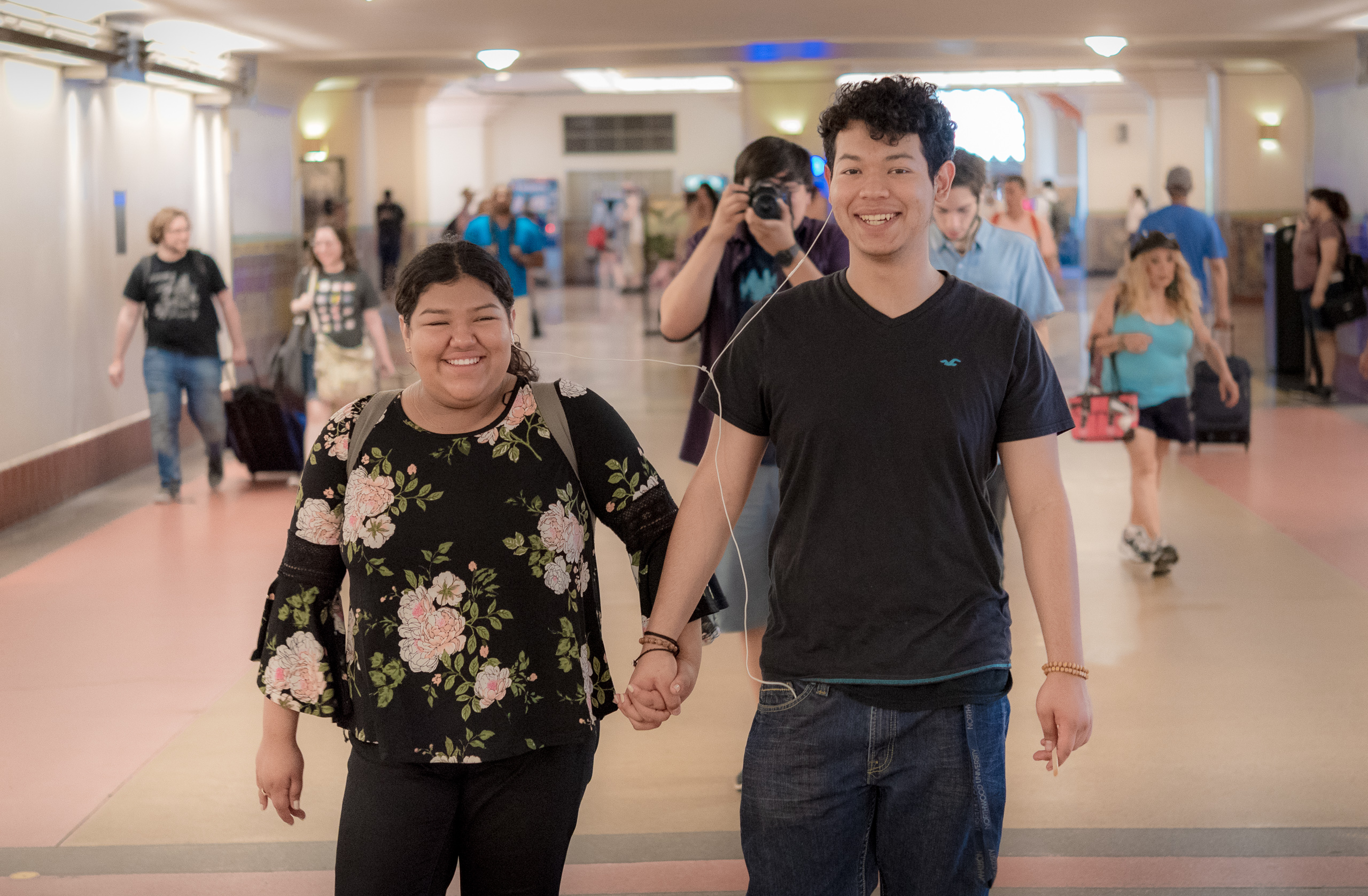 a couple walking through the terminal at Union Station and sharing a pair of earbuds. In-between and behind them a photographer points a camera at me