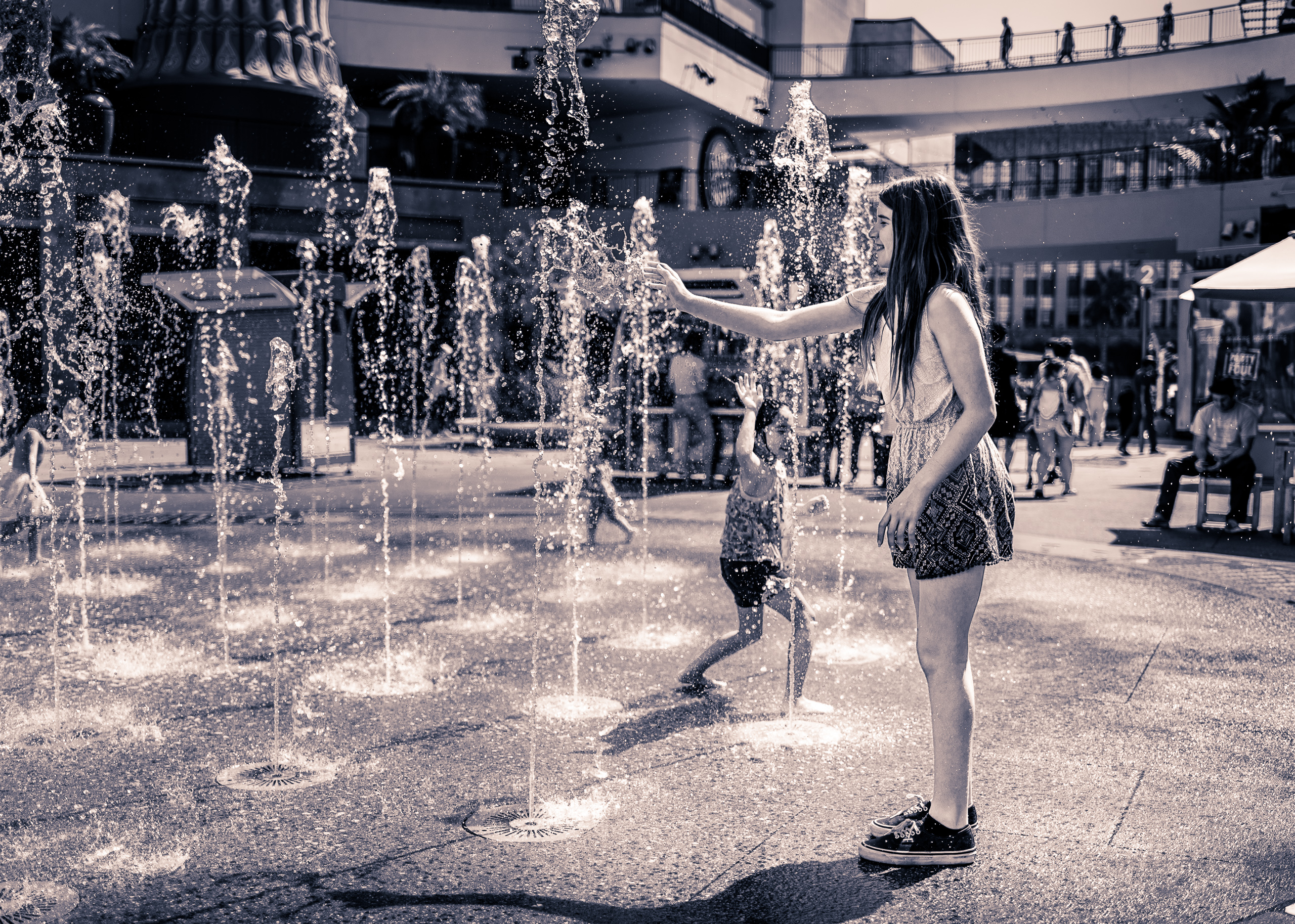 at the Hollywood & Highland water fountain, a young girl extends her hand to feel the water on a hot day in Hollywood