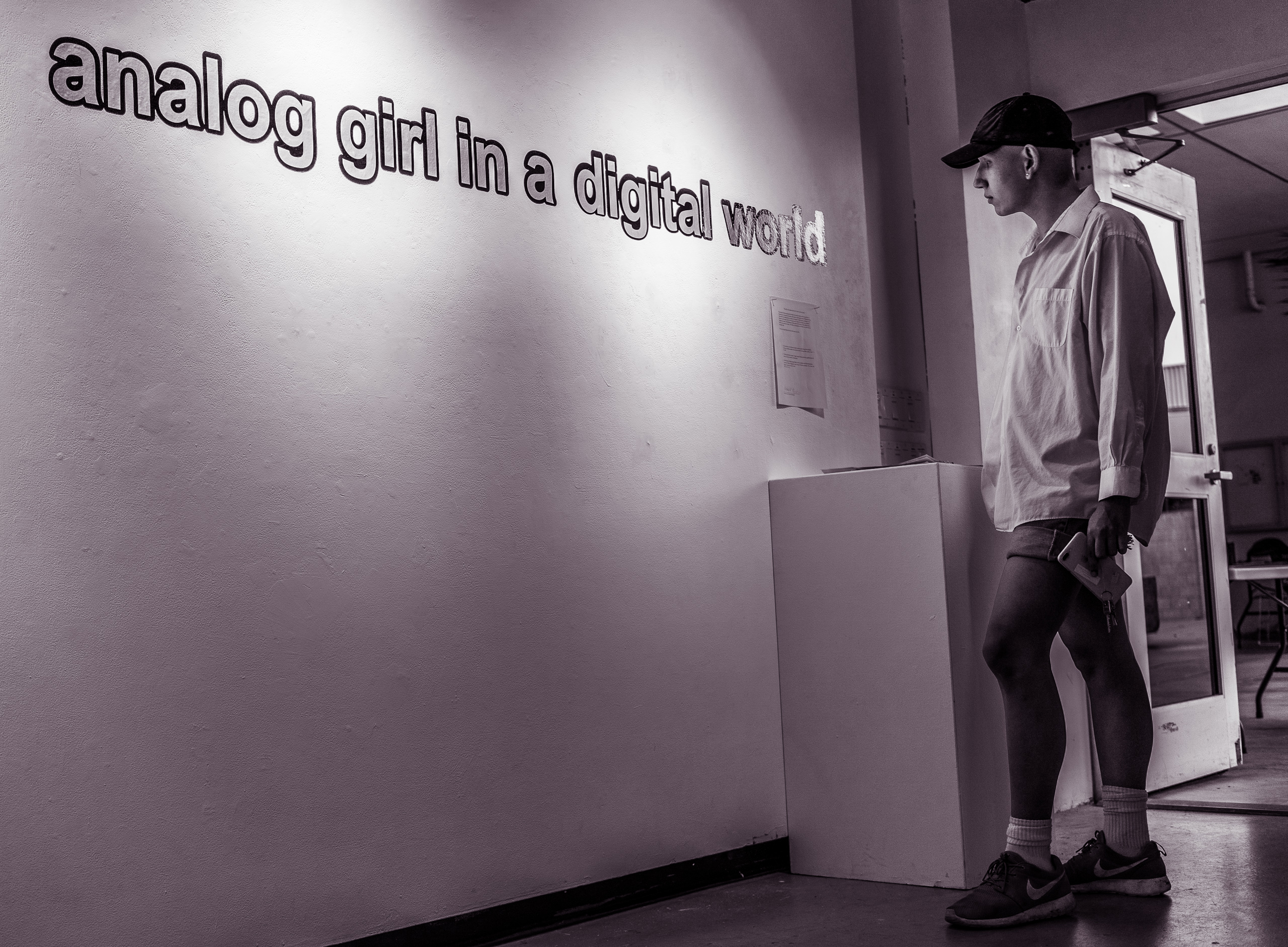 a visitor to the gallery reads the artist's statement on the wall. Next to him is the title of the exhibition on the wall, "analog girl in a digital world"