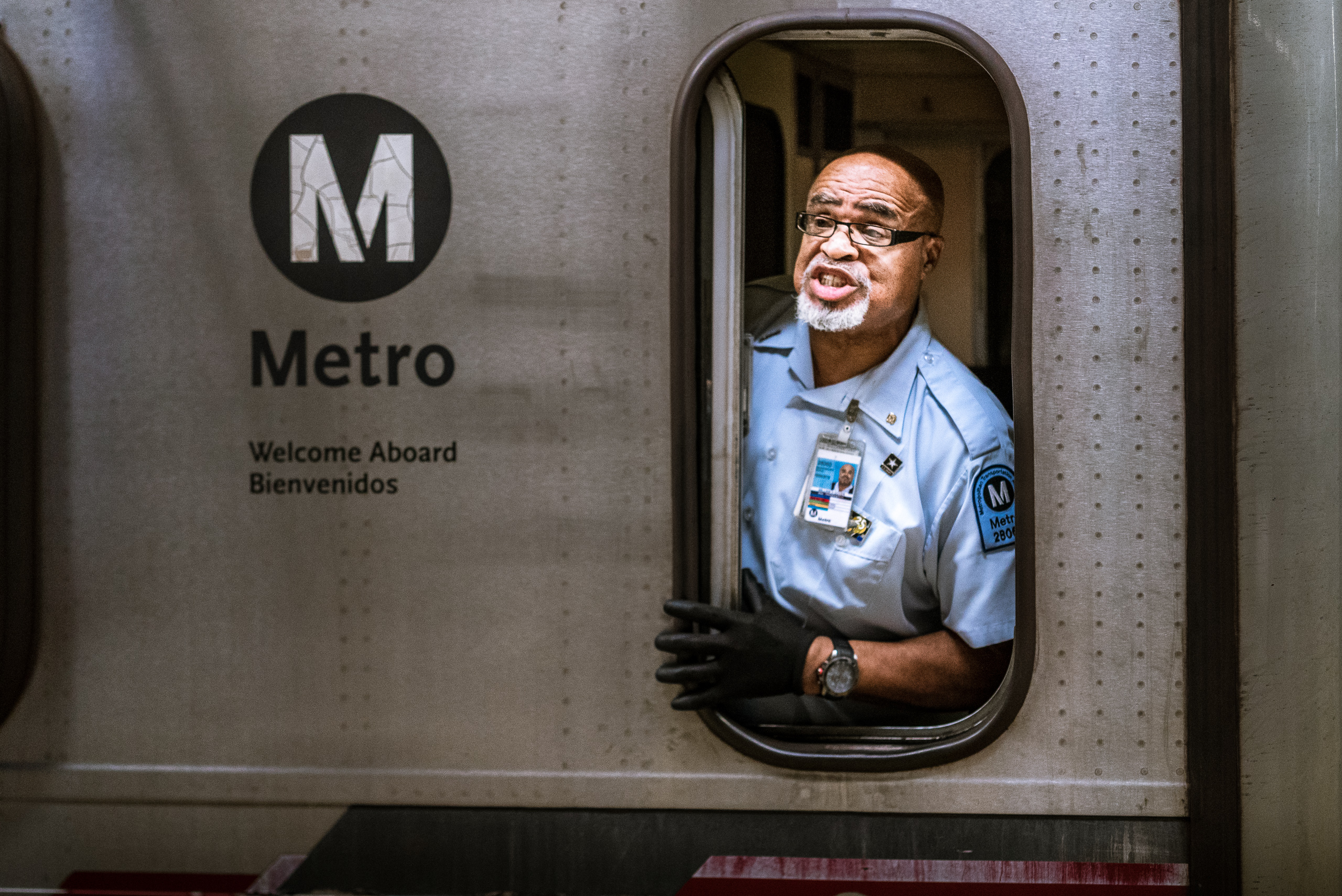 a Metro Red Line engineer sticks his head out the small, vertical window of the train's engine room to give information to travelers