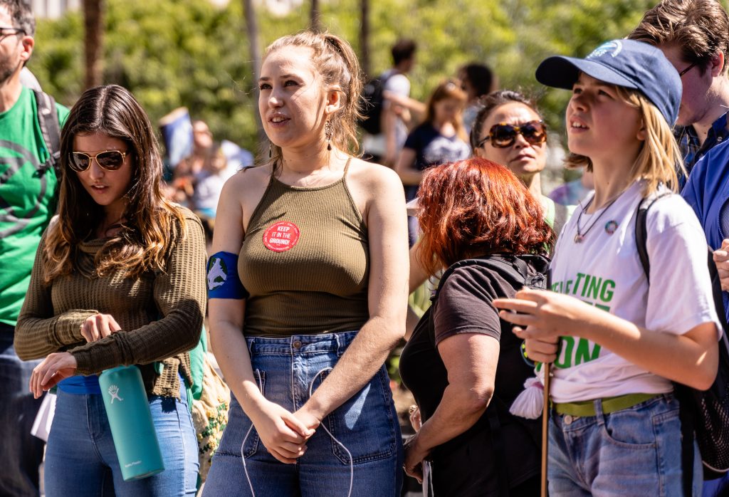 Los Angeles Youth Climate March organizer Arielle Martinez-Cohen (center), 17, a senior at New West Charter School in West Los Angeles listens to speakers in front of Los Angeles City Hall on Friday, March 15, 2019. Of the march, Martinez-Cohen said, "It’s super exciting to see all these students fighting for the same cause." When asked what comes next, she offered, "We want to bring our demands to our city hall legislators. We want to have Los Angeles carbon neutral by 2030. We’re on schedule for 2045, but that’s not soon enough. The City of Los Angeles has been taking the initiative, and we don’t want to spread hate, we want to spread love. But we can’t wait till 2045. We have to be 100% carbon neutral by 2030." (Glenn Zucman/The Corsair)