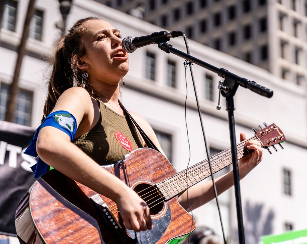 Los Angeles Youth Climate March organizer Arielle Martinez-Cohen, 17, a senior at New West Charter School in West Los Angeles performs for students and other climate marchers in front of Los Angeles City Hall on Friday, March 15, 2019. Of the march, Martinez-Cohen said, "It’s super exciting to see all these students fighting for the same cause." When asked what comes next, she offered, "We want to bring our demands to our city hall legislators. We want to have Los Angeles carbon neutral by 2030. We’re on schedule for 2045, but that’s not soon enough. The City of Los Angeles has been taking the initiative, and we don’t want to spread hate, we want to spread love. But we can’t wait till 2045. We have to be 100% carbon neutral by 2030." (Glenn Zucman/The Corsair)
