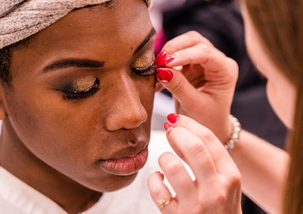 Kaia Cobb, 34, From Houston, Texas, Applies A False Eyelash To Skye Johnson, 18, A Brooklyn, NY Born, And Raleigh, NC Raised, Student In The SMC Esthetician Program At The SMC Cosmetology Salons In The Business Building On SMC’s Main Campus On Thursday, April 18, 2019. In Addition To The Esthetician Program, Johnson Is Also Taking His Nursing Prerequisites At SMC With The Goal Of Becoming A Medical Aesthetician. Medical Aestheticians Provide Skin Care In Medical Settings And Can Assist With Injectables Like Botox. Cobb Holds A 2007 BBA In Economics From Baylor University In Waco, Texas. She Enrolled In The Esthetician Program At SMC To Pursue Her "Teenage Dream Of Being A Makeup Artist In Los Angeles." (Glenn Zucman/The Corsair)