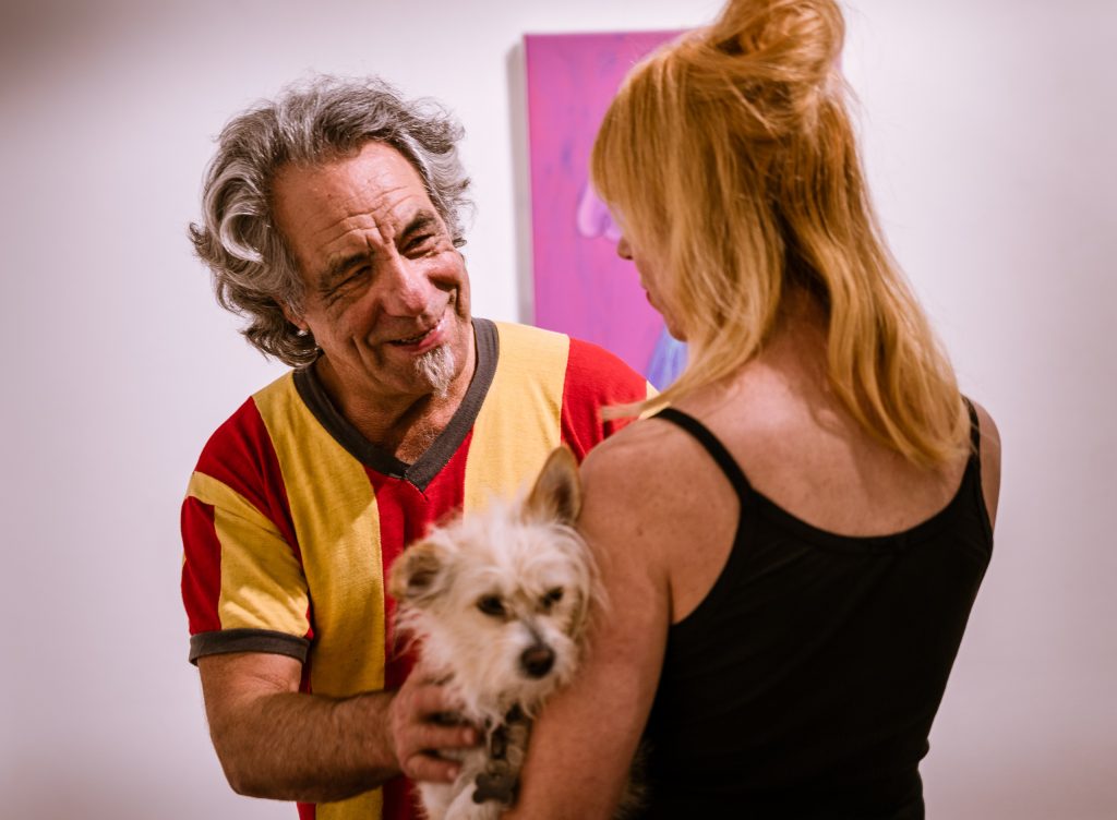 La Luz De Jesus Gallery Owner Billy Shire Talks With Friend And Owner-Instructor At Glendale Yoga, Laura Bogner, Who Holds Shire's Dog "Floyd Shire" At The Opening For In Memory Of Water And Onward At La Luz De Jesus Gallery On Friday, May 3, 2019. Two Shows Are Running At La Luz De Jesus From May 3 To June 2: Matthew Couper's Solo Exhibition In Memory Of Water, And The Group Portrait Show Onward Featuring Artists Michele Melcher, Baldur Helgason, Yeo Kaa, Valery Pobjoy, And Sung Jik Yang. (Glenn Zucman/The Corsair)