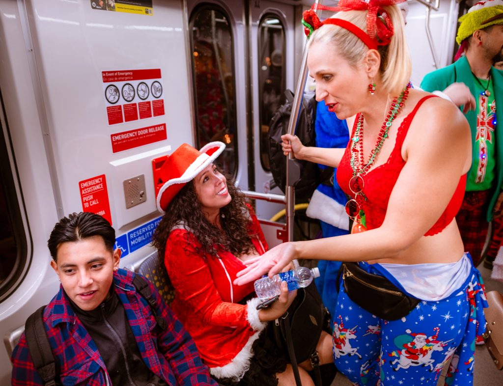 A woman dressed for Santacon 2018 rides the Metro Gold line and lectures a young man that he needs to "Call his mother"